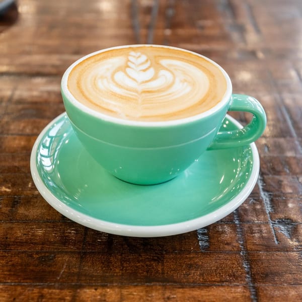 La Finca Coffee & Bakery latte in a teal cup with intricate latte art on a wooden table.