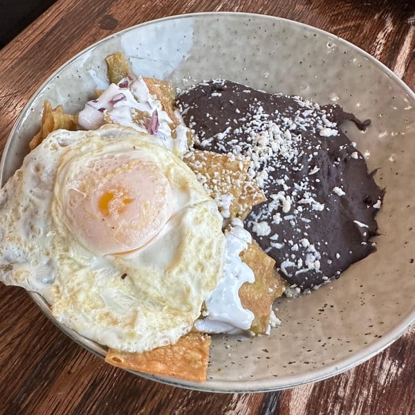 Chilaquiles with a fried egg, black beans, and crema on a speckled plate at La Finca.