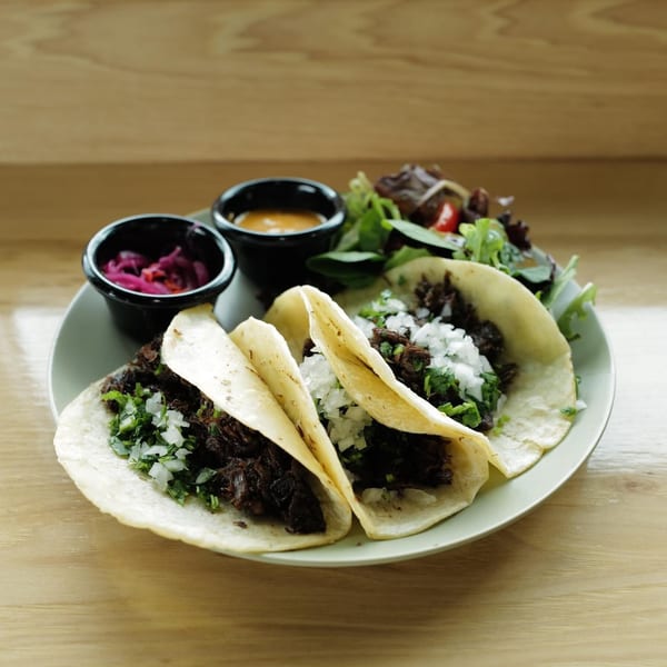 Three beef tacos with onions and cilantro, served with pickled onions, sauce, and a side salad.