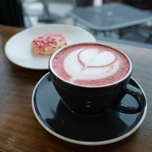 A La Finca pink latte with heart art and a cookie with pink sprinkles on a wooden table.