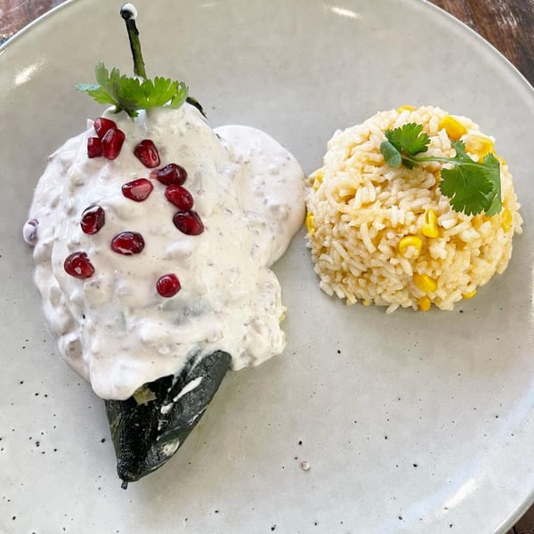 Chiles en nogada with pomegranate seeds and cilantro, served with a side of rice and corn.