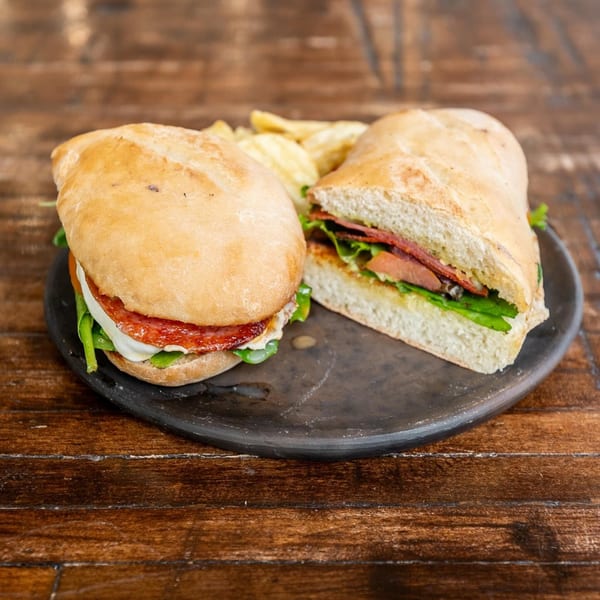 Two halves of a La Finca sandwich with salami, cheese, and greens on a dark plate with chips.